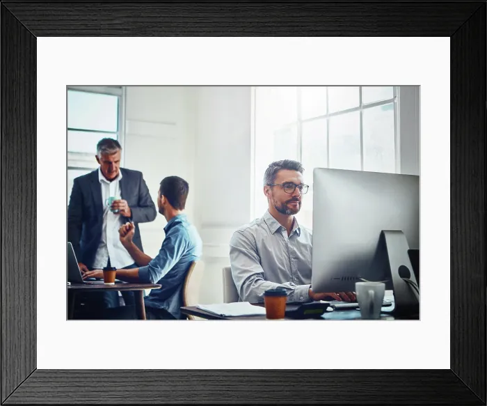 Framed Print : Computer, work and businessman with his colleagues in the background talking Framed Print : Computer, work and businessman with his colleagues in the background talking