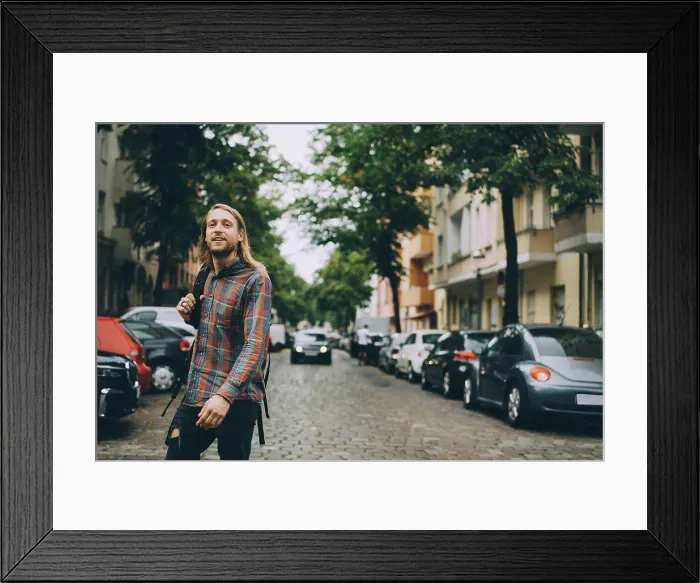 Framed Print : Young man carrying backpack while walking on cobbled street amidst cars in city