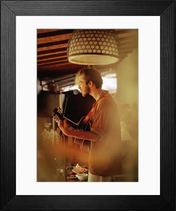 Framed Print : Young man musician plays the guitar and sings into a microphone