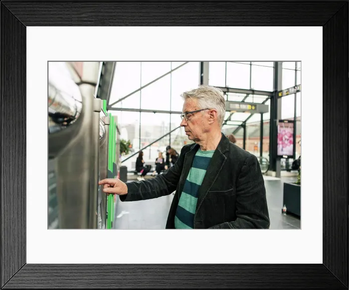 Framed Print : Senior male commuter using kiosk at railroad station