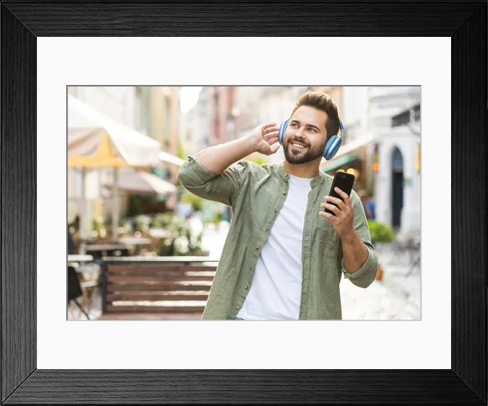 Framed Print : Happy young man in wireless headphones choosing, listening music in smartphone dancing outdoors Framed Print : Happy young man in wireless headphones choosing, listening music in smartphone dancing outdoors