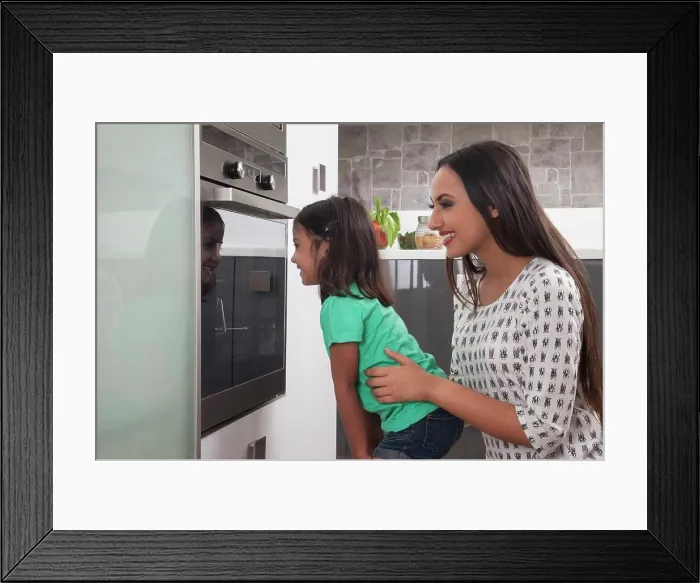 Framed Print : Young mother and daughter looking into an oven Framed Print : Young mother and daughter looking into an oven