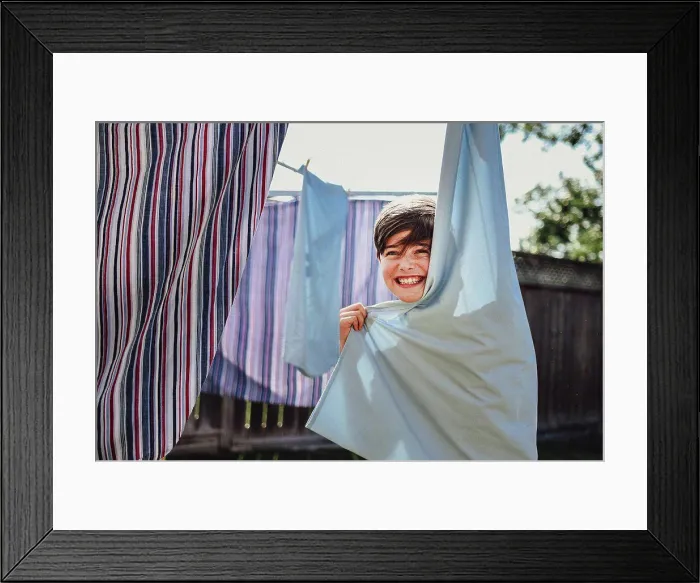 Framed Print : Happy boy hiding behind clothes hanging on a clothesline outside