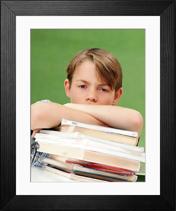 Framed Print : Schoolboy with a stack of books, looking frustrated, tired Framed Print : Schoolboy with a stack of books, looking frustrated, tired