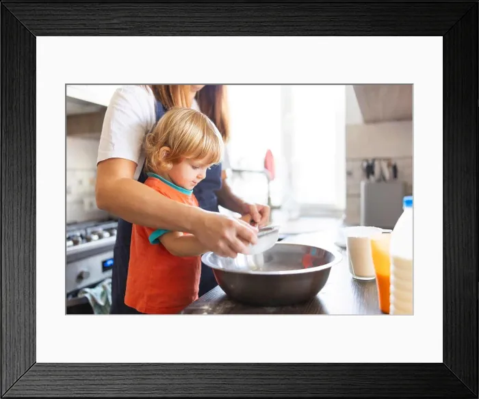 Framed Print : Family in a kitchen. Mother and child sieving flour into a bowl