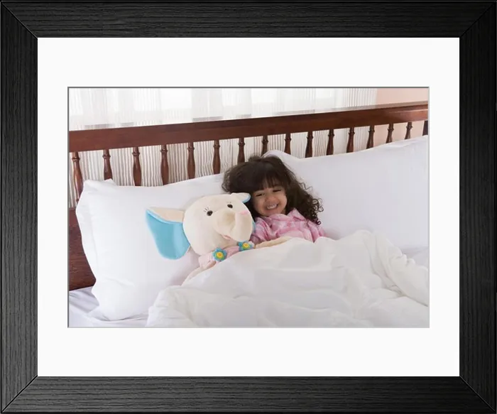 Framed Print : Girl (3-4) lying on bed by toy, smiling Framed Print : Girl (3-4) lying on bed by toy, smiling