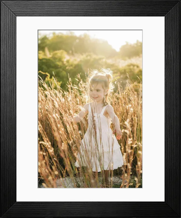 Framed Print : Smiling young girl in a white dress walking through tall grass