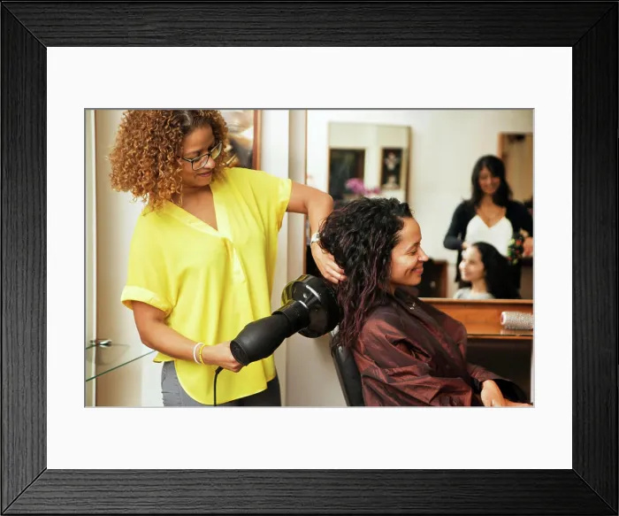 Framed Print : Stylist blowdrying a happy client's hair at a cozy salon