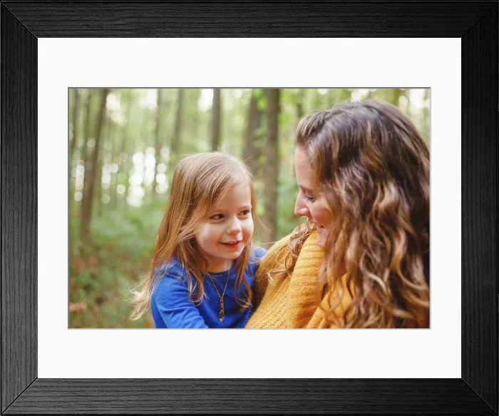 Framed Print : A little girl snuggles in her mother's arms as they smile together Framed Print : A little girl snuggles in her mother's arms as they smile together