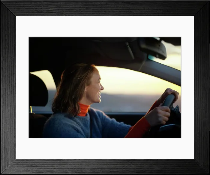 Framed Print : Smiling woman driving a car during sunset with warm light illuminating her face Framed Print : Smiling woman driving a car during sunset with warm light illuminating her face