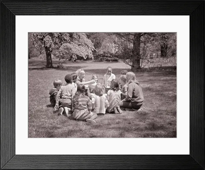 Framed Print : 1960s ADULT WOMAN TEACHER HANDING A BALL TO ETHNICALLY MIXED GROUP OF CHILDREN VARIOUS AGES SITTING IN CIRCLE ON THE Framed Print : 1960s ADULT WOMAN TEACHER HANDING A BALL TO ETHNICALLY MIXED GROUP OF CHILDREN VARIOUS AGES SITTING IN CIRCLE ON THE
