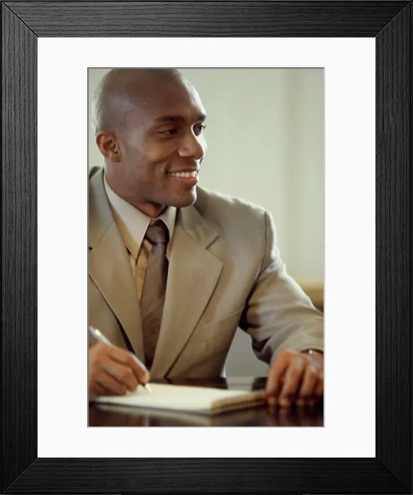 Framed Print : Portrait of a businessman seated at an office desk writing in a notepad Framed Print : Portrait of a businessman seated at an office desk writing in a notepad