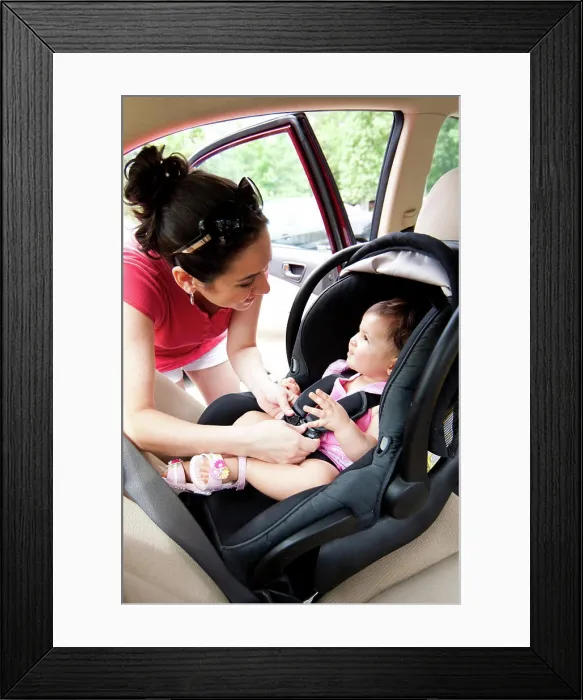 Framed Print : Baby in car seat for safety Happy smiling mother placing baby in car seat and closing belt for safety Framed Print : Baby in car seat for safety Happy smiling mother placing baby in car seat and closing belt for safety