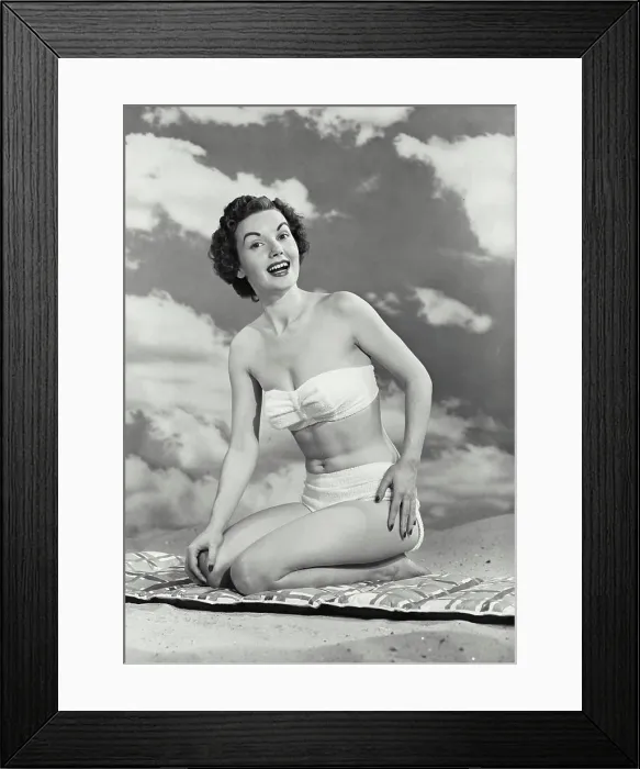 Framed Print : Vintage photograph. Woman smiling in swimsuit kneeling on mat in sand Framed Print : Vintage photograph. Woman smiling in swimsuit kneeling on mat in sand