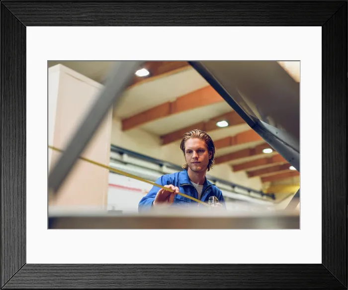 Framed Print : Focused young man using measurement tape to find length in factory Framed Print : Focused young man using measurement tape to find length in factory