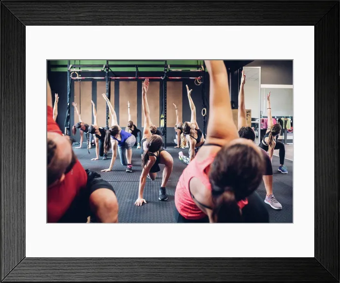 Framed Print : Group of women training in gym with male trainer, bending forward with arm raised