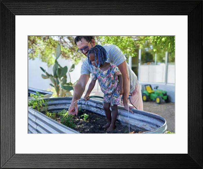 Framed Print : Father and cute daughter watering plants in backyard
