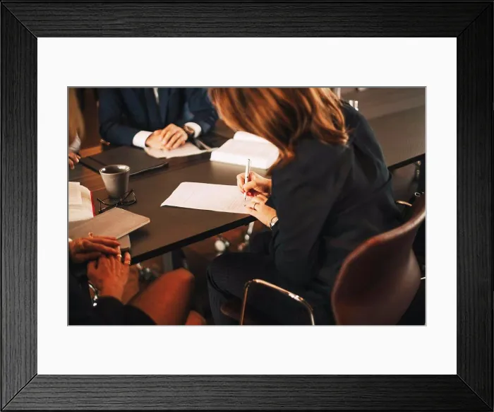 Framed Print : Female lawyer signing documents while sitting in meeting with colleagues at office Framed Print : Female lawyer signing documents while sitting in meeting with colleagues at office