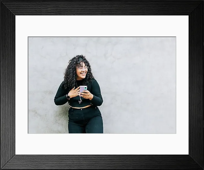 Framed Print : Young latin woman happy with her cell phone leaning against a wall Framed Print : Young latin woman happy with her cell phone leaning against a wall