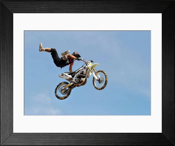 Framed Print : A motocross rider performing a stunt while flying through the air on his motorcycle in a blue sky background Framed Print : A motocross rider performing a stunt while flying through the air on his motorcycle in a blue sky background