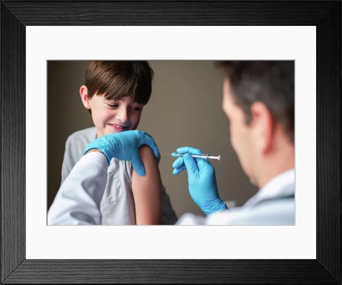 Framed Print : Nervous looking child getting vaccinated by doctor holding a needle Framed Print : Nervous looking child getting vaccinated by doctor holding a needle