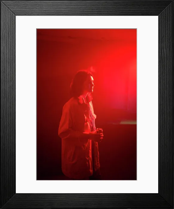 Framed Print : A woman stands in a red-lit room holding a drink Framed Print : A woman stands in a red-lit room holding a drink