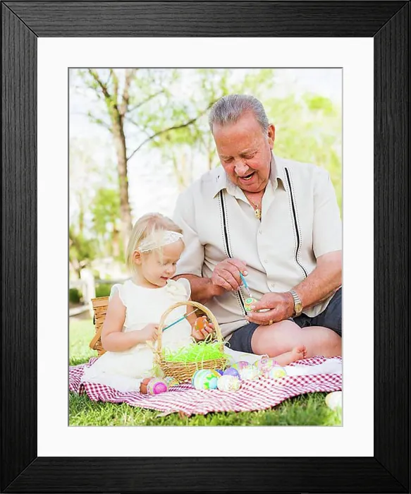 Framed Print : Loving grandfather and granddaughter coloring easter eggs together on picnic blanket at the park