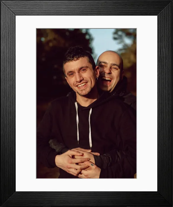Framed Print : Cheerful homosexual couple embracing on walkway in forest in sunny day on blurred background