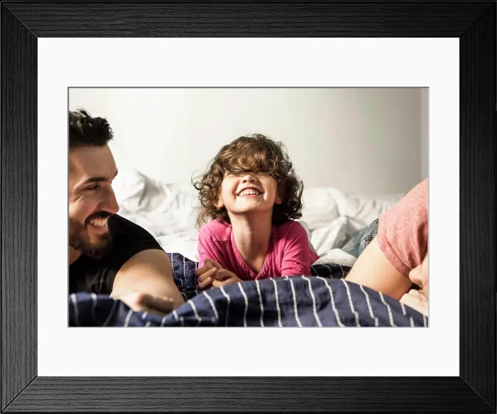 Framed Print : Fathers looking at cheerful daughter playing on bed at home Framed Print : Fathers looking at cheerful daughter playing on bed at home