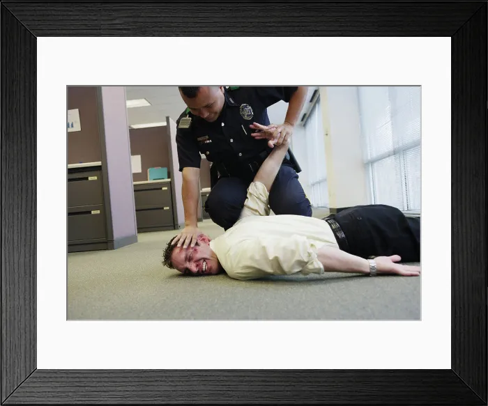 Framed Print : Police officer holding beat up businessman on floor in office Framed Print : Police officer holding beat up businessman on floor in office