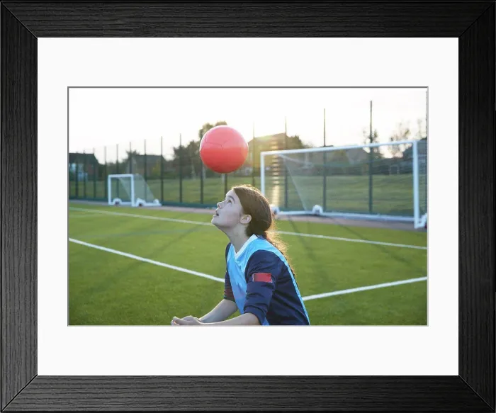 Framed Print : UK, Female soccer player bouncing ball in field at sunset Framed Print : UK, Female soccer player bouncing ball in field at sunset