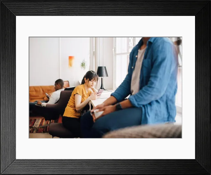Framed Print : Female programmer using mobile phone on desk while sitting in office Framed Print : Female programmer using mobile phone on desk while sitting in office