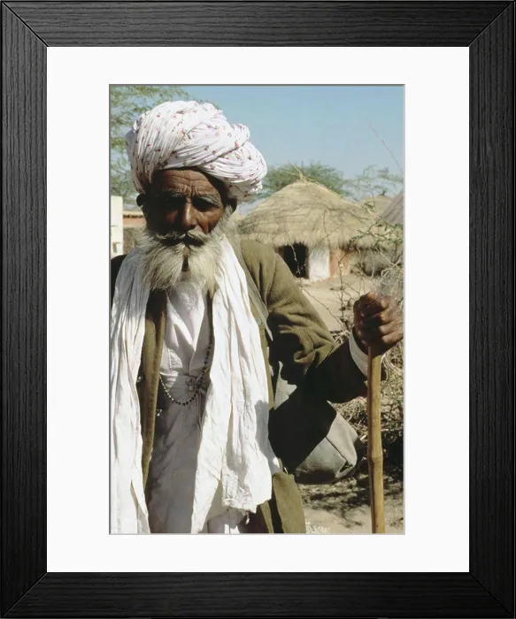 Framed Print : India, Rajasthan, Senior local man leaning on cane, village houses in background Framed Print : India, Rajasthan, Senior local man leaning on cane, village houses in background