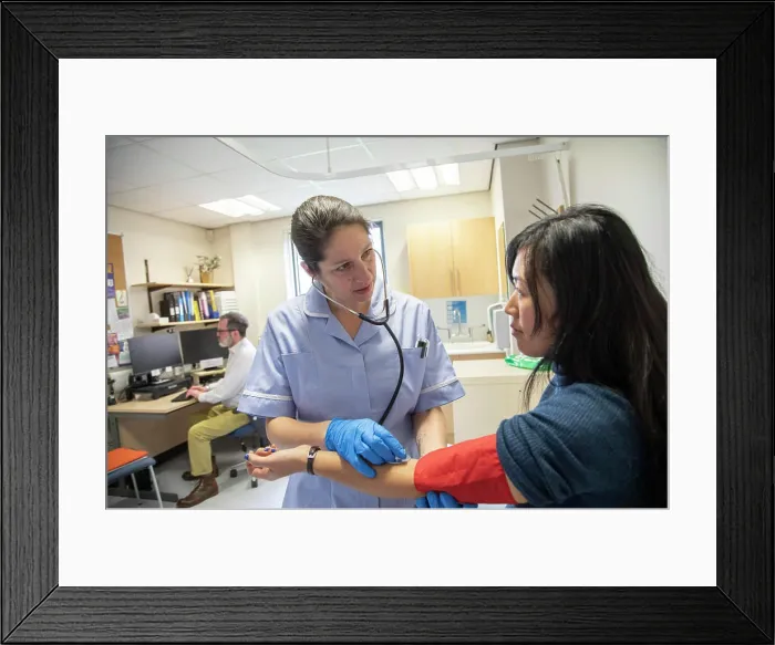 Framed Print : Nurse examining a patient's arm for blood pressure and pulse