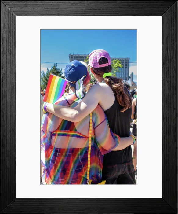 Framed Print : LGBTQ couple at a Pride event, embracing with flags Framed Print : LGBTQ couple at a Pride event, embracing with flags