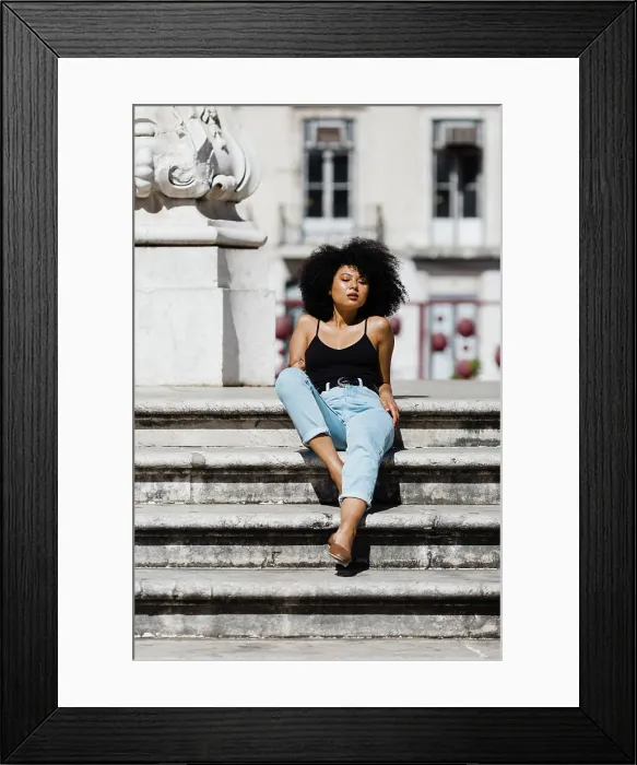 Framed Print : Beautiful ethnic woman in jeans and tank top relaxing and sunbathing on stone stairs against urban background