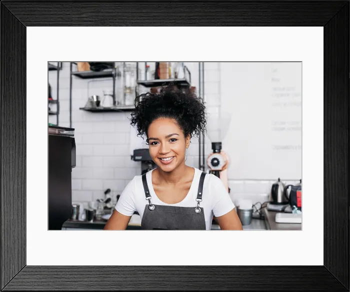 Framed Print : Nahaufnahme einer jungen lächelnden Barista mit lockigem Haar und Schürze Close-up of a young smiling barista with Framed Print : Nahaufnahme einer jungen lächelnden Barista mit lockigem Haar und Schürze Close-up of a young smiling barista with