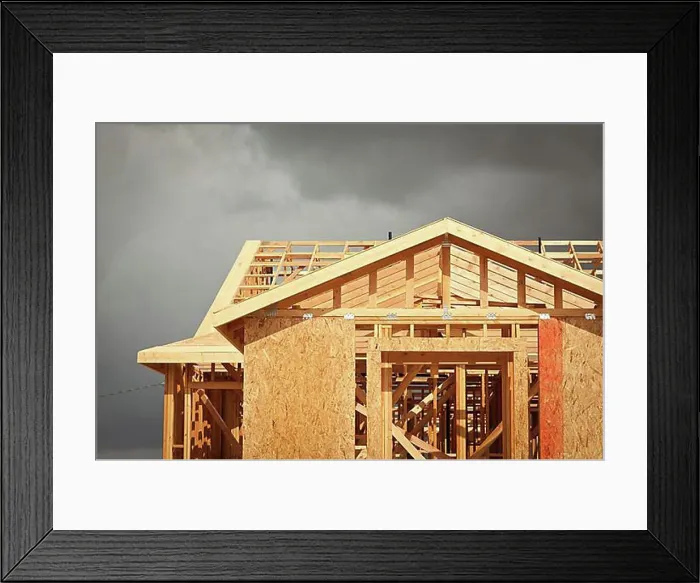 Framed Print : Home construction framing with ominous grey clouds behind Framed Print : Home construction framing with ominous grey clouds behind
