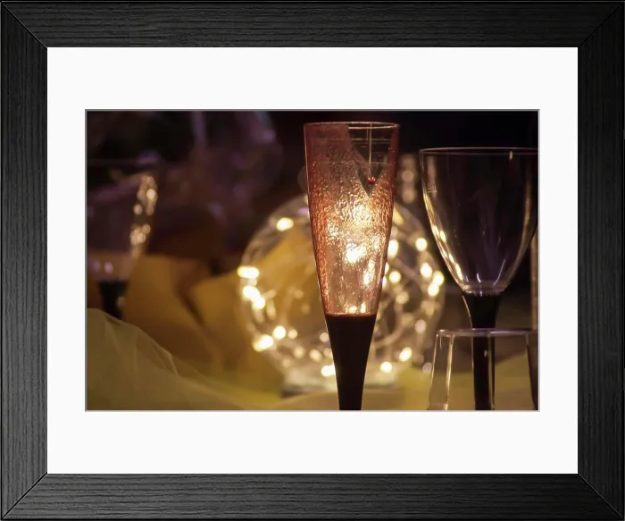 Framed Print : Romantic atmosphere created by a champagne flute and a wine glass illuminated by warm string lights