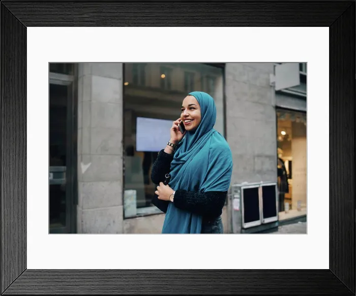Framed Print : Happy young Muslim woman talking on mobile phone walking building in city