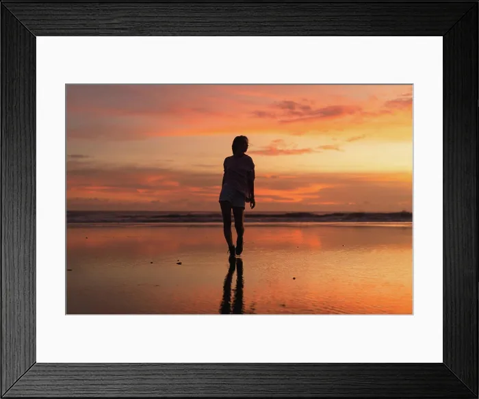 Framed Print : Young woman with arms raised facing colorful sunset at low tide beach