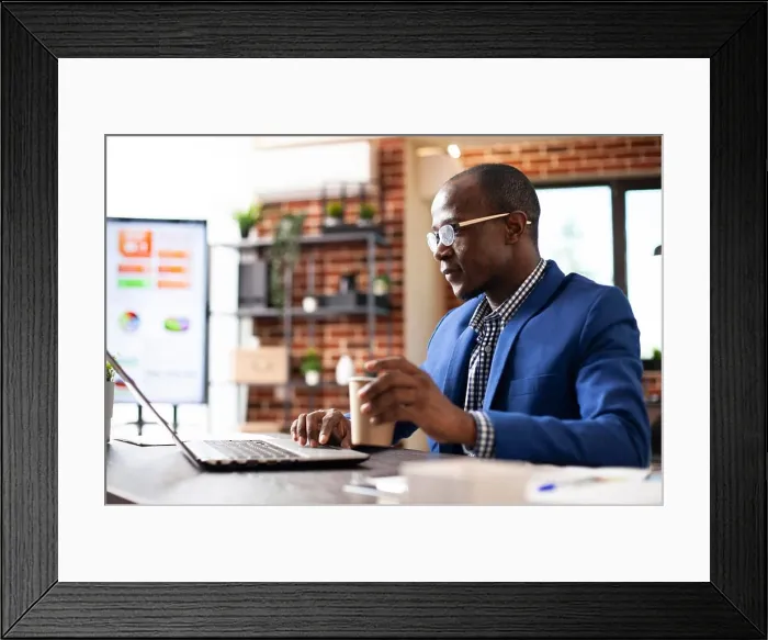 Framed Print : Male employee holding paper cup and working on his personal computer in startup office Framed Print : Male employee holding paper cup and working on his personal computer in startup office
