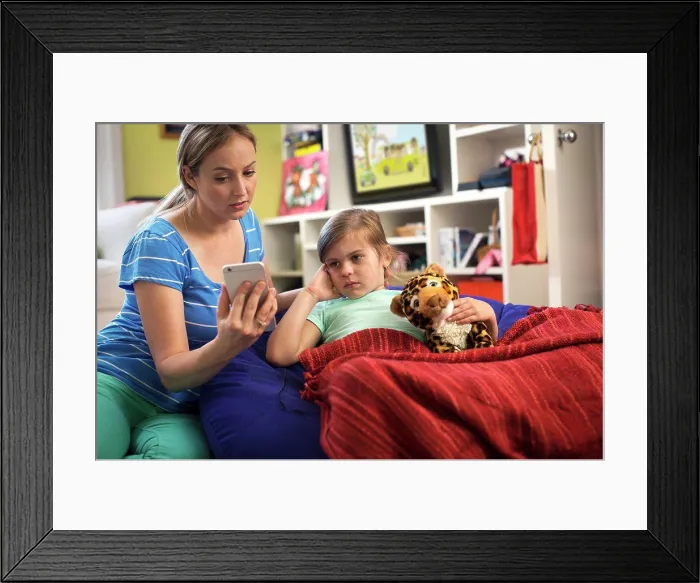 Framed Print : Mom with daughter who is not feeling well using cell phone to consult doctor and get advice via Telemedicine service