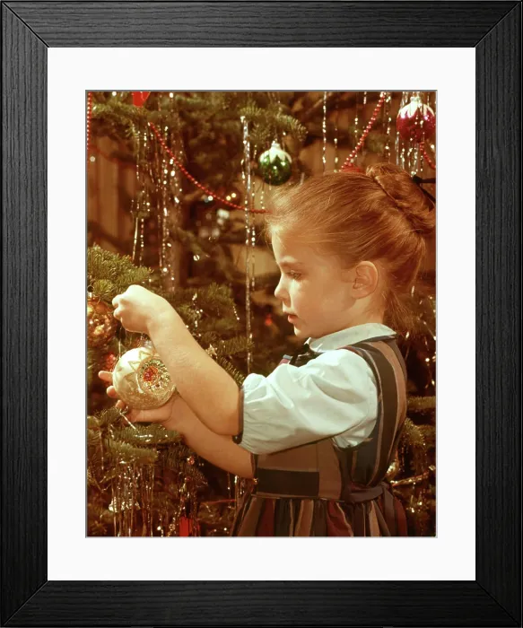 Framed Print : 1960s PROFILE SERIOUS LITTLE GIRL HANGING GLASS ORNAMENT ON CHRISTMAS TREE BRANCH Framed Print : 1960s PROFILE SERIOUS LITTLE GIRL HANGING GLASS ORNAMENT ON CHRISTMAS TREE BRANCH
