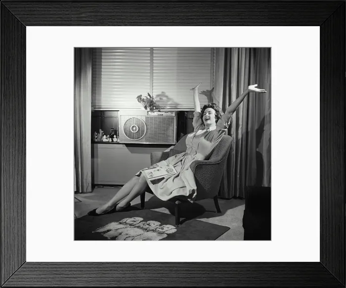 Framed Print : Young woman sitting in an armchair with her arms raised Framed Print : Young woman sitting in an armchair with her arms raised