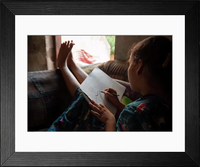 Framed Print : girl sitting on the sofa and drawing on a paper