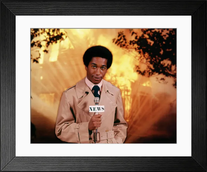 Framed Print : 1970s AFRICAN AMERICAN MAN TELEVISION NEWS REPORTER WEARING RAINCOAT SPEAKING INTO MICROPHONE AT FIRE SCENE LOOKING AT