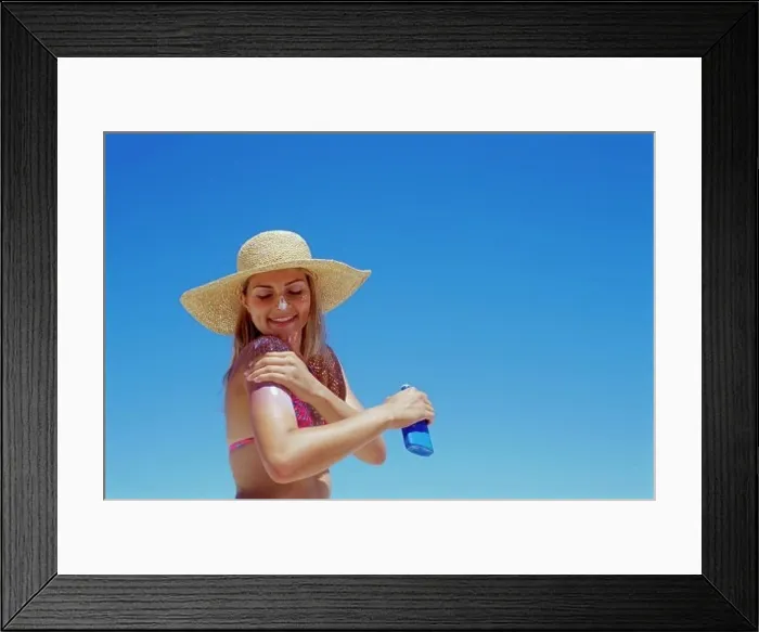 Framed Print : Side profile of a young woman applying suntan lotion on her arm Framed Print : Side profile of a young woman applying suntan lotion on her arm