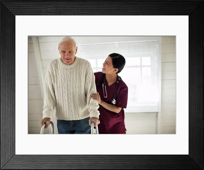 Framed Print : Smiling female nurse encouraging an elderly male patient as he uses a walking frame