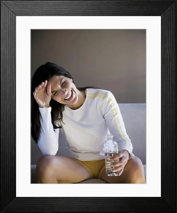 Framed Print : Woman sitting on sofa with bottled water smiling Framed Print : Woman sitting on sofa with bottled water smiling